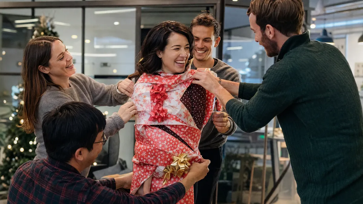 Colleagues wrapping a teammate in wrapping paper during a holiday party game