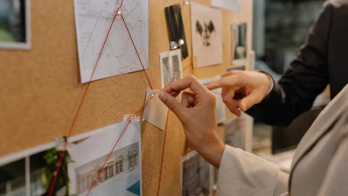 Hands connecting escape room clues with string on a corkboard