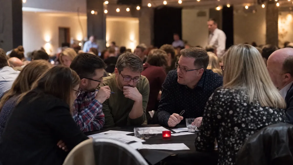 Teams whispering over trivia answer sheets at round tables