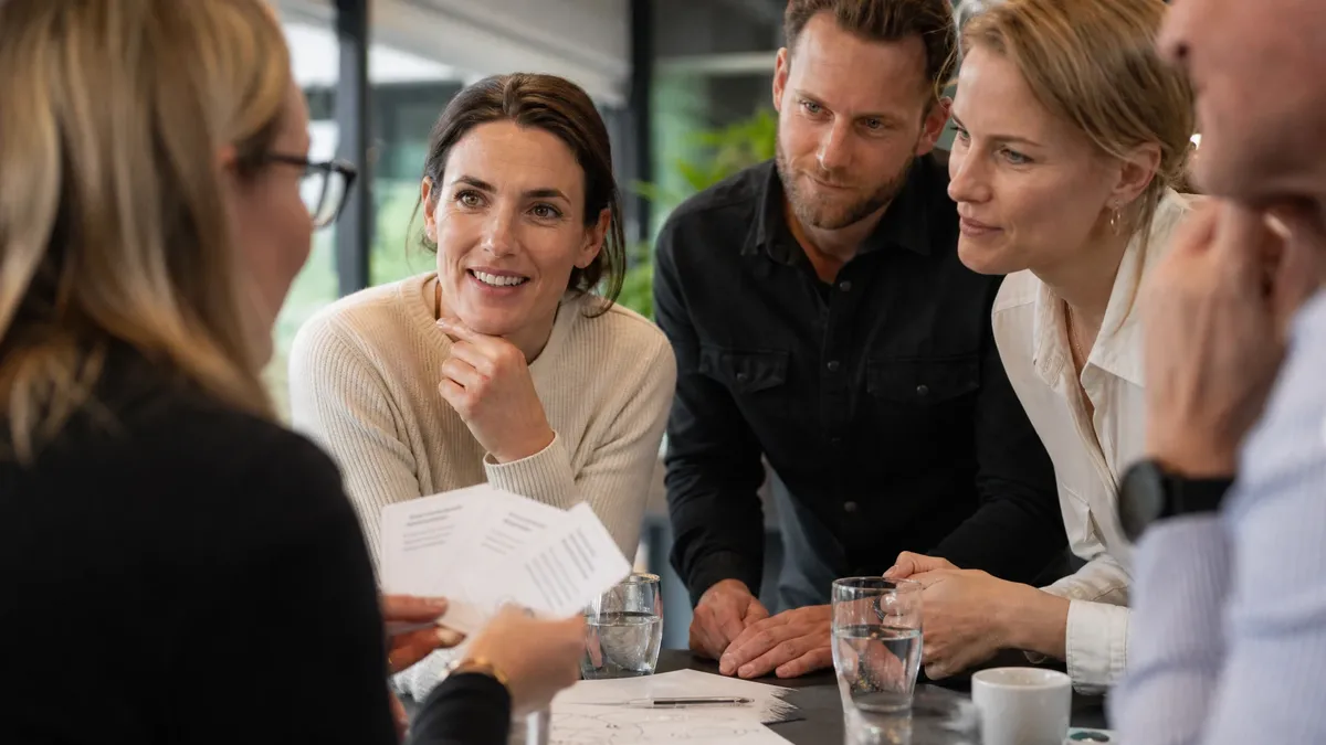 Facilitator holding icebreaker question cards with a team gathered around a standing table