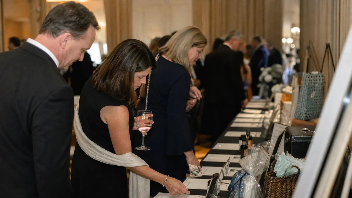 Elegant silent auction display table at a gala with guests writing bids