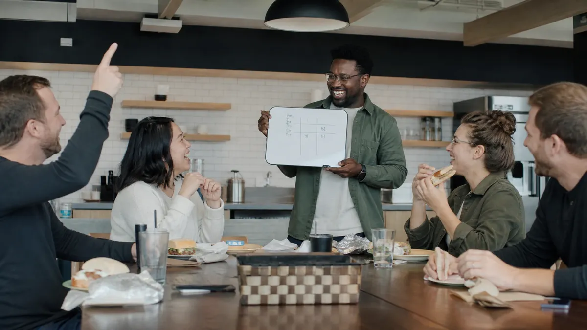 Lunchtime team trivia in an office kitchen with a whiteboard scoreboard