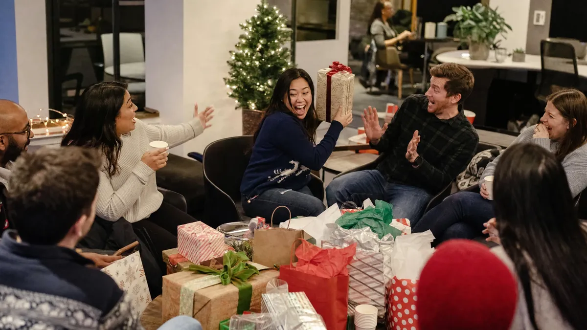 Coworkers laughing as one steals a wrapped gift during a white elephant exchange